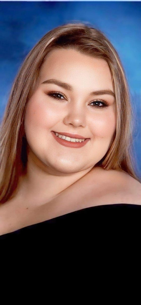 Portrait of Marissa Caitlyn Ladatto smiling, with long light-brown hair, against a blue background